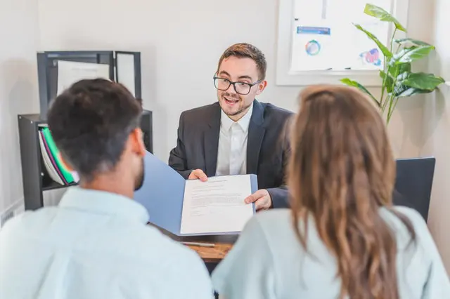 Man in Suit Offering Folder to Couple